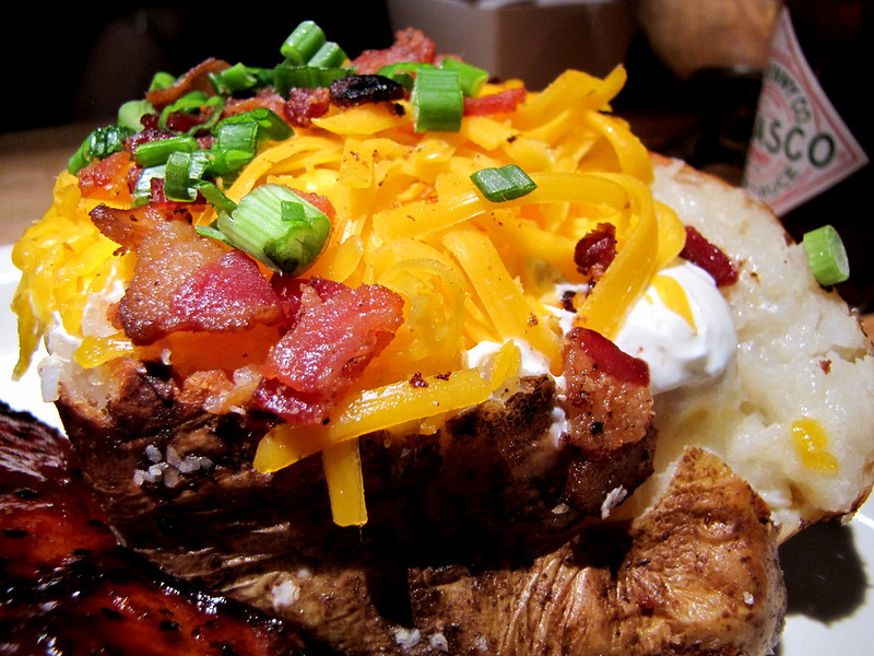 Loaded baked potato topped with cheddar cheese, sour cream, bacon, and green onions